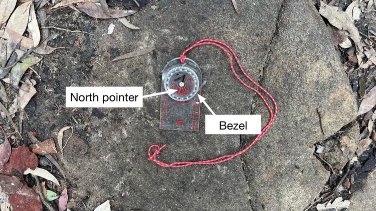 Compass lying on a rock with labels showing the north pointer and bezel